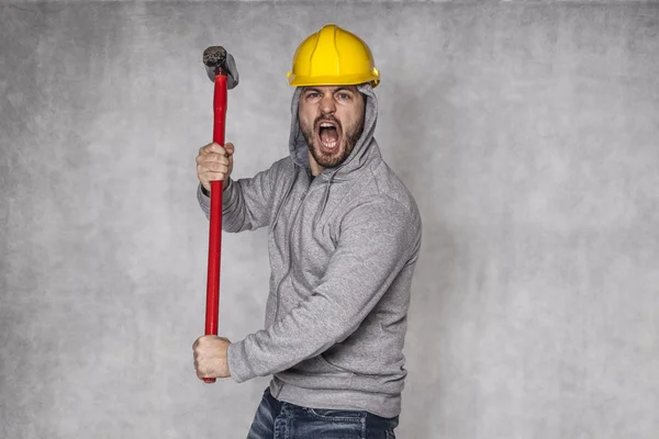 Bouwer op een grijze achtergrond, een hamer holding en schreeuwen — Stockfoto