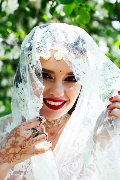 young pretty indian girl in jewelry and veil posing cheerful happy smiling in green park, lifestyle people concept