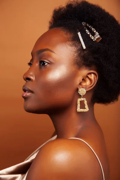 young pretty african model with golden jewelry in fashion style dress smiling happy on brown backround, lifestyle people concept