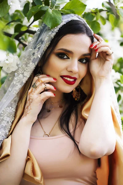 young pretty indian girl in jewelry and veil posing cheerful happy smiling in green park, lifestyle people concept