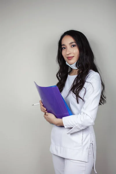 young asian woman doctor in white uniform gesturing positive on gray background, wearing a mask, lifestyle healthcare people concept