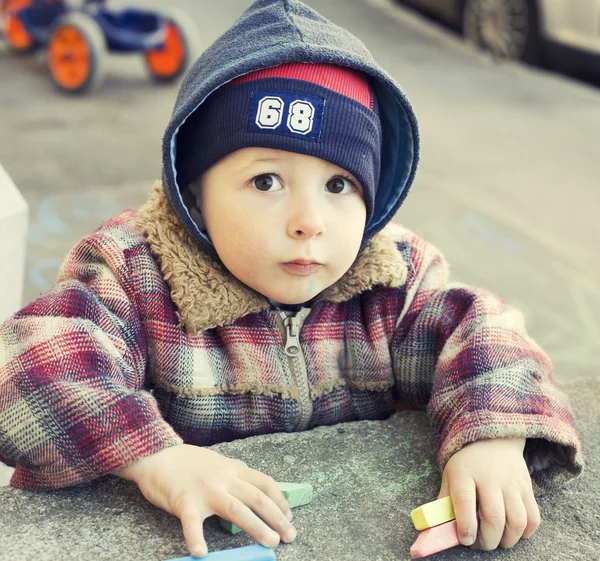 portrait of little cute boy writing with chalk on the ground