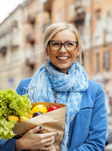 young pretty blond woman with food in bag walking on street