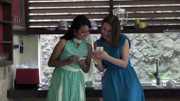 Подружки разговаривают и используют смартфон на кухне — стоковое видео