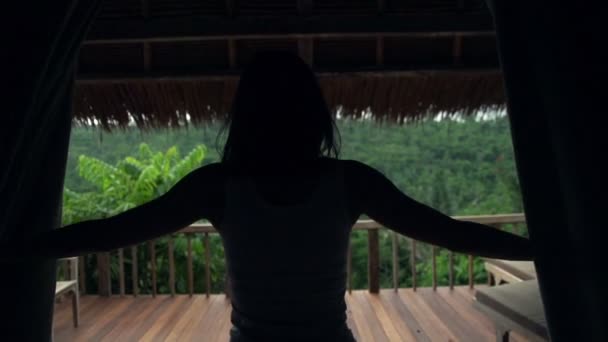 Женщина обнажает занавески и вытягивает руки на террасе — стоковое видео