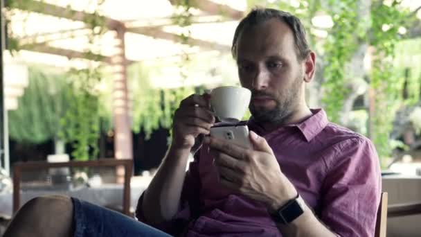 Ο άνθρωπος γραπτών μηνυμάτων και πίνοντας τον καφέ στην καφετέρια — Αρχείο Βίντεο