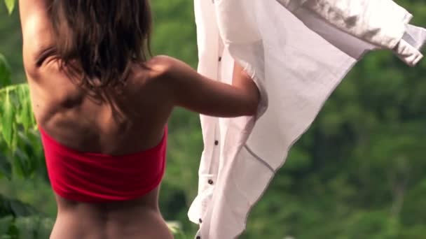 Молодая женщина надевает рубашку на террасу — стоковое видео