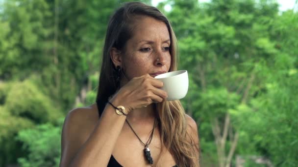 Задумчивая женщина пьет кофе в саду — стоковое видео