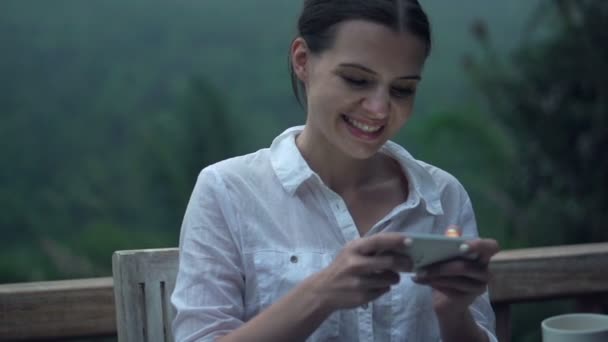 Woman playing game on smartphone on terrace — Stock Video