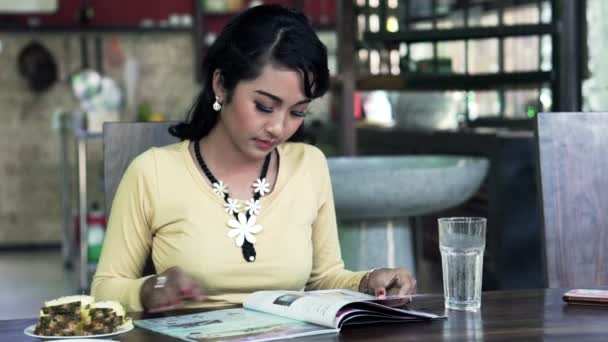 Kobieta czytająca magazyn i jedzenie ananasa przez tabela — Wideo stockowe