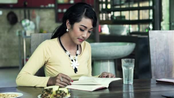 Woman reading book and using smartphone by table — Stock Video