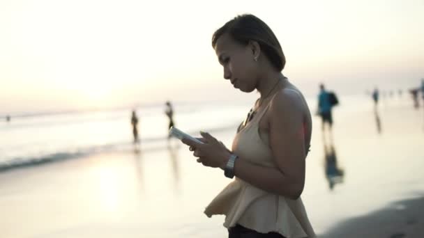 Mulher com smartphone durante o pôr do sol na praia — Vídeo de Stock