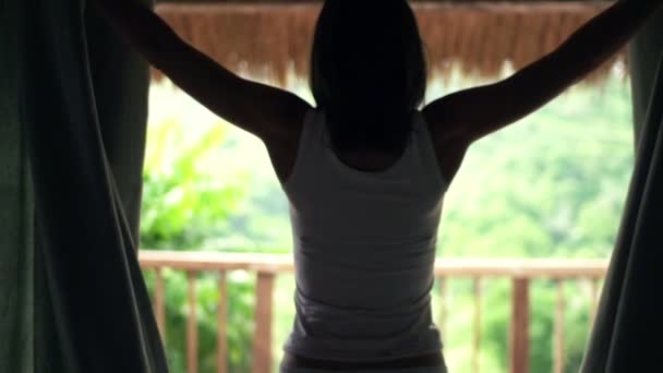 Vrouw onthullen gordijnen en stretching wapens op terras — Stockvideo
