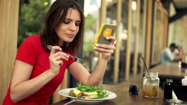 Woman using smartphone and eating salad — Stock Video