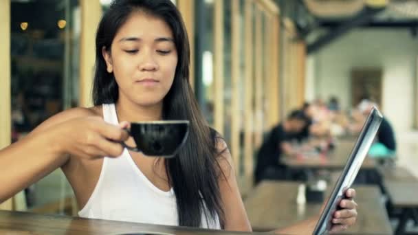 Женщина читает что-то на планшетном компьютере и пьет кофе — стоковое видео