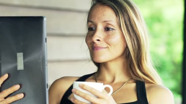 Mujer leyendo algo en la computadora de la tableta y beber café — Vídeos de Stock