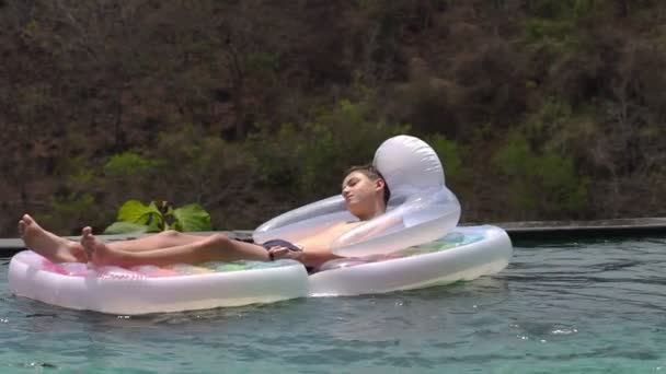 Teenager relaxing on floating mattress in swimming pool — Stock Video