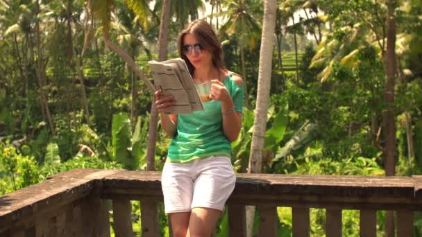 Kvinna dricker kaffe och läsa tidningen på terrassen — Stockvideo