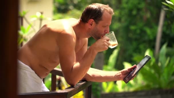 Ο άνθρωπος χρησιμοποιώντας τον υπολογιστή tablet και πίνοντας καφέ στη βεράντα — Αρχείο Βίντεο