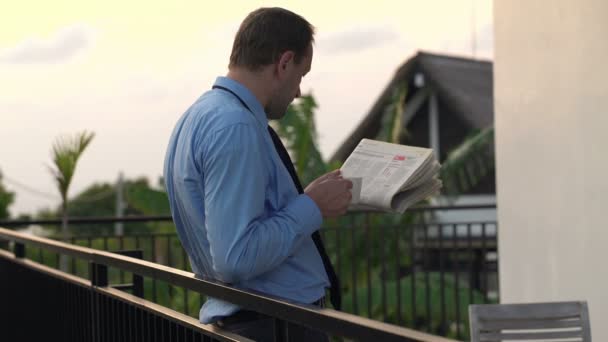 Бизнесмен читает газеты и пьет на террасе — стоковое видео