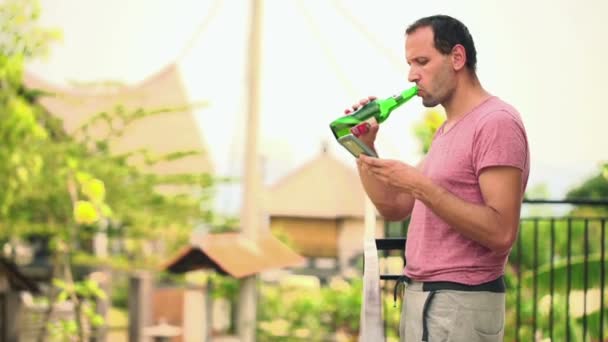 Мужчина со смартфоном, пьет пиво на террасе — стоковое видео