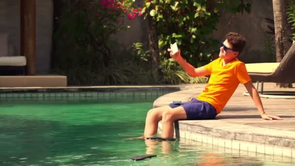 Menino tirando foto com celular na borda da piscina — Vídeo de Stock