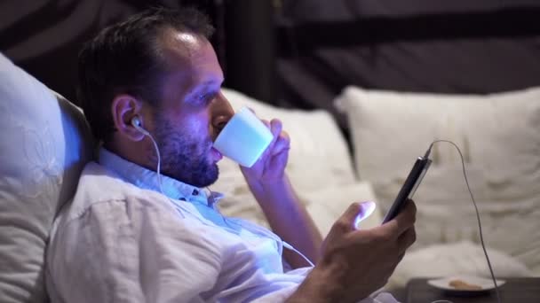 남자는 침대에 자신의 스마트폰에 음악을 듣으십시오 — 비디오