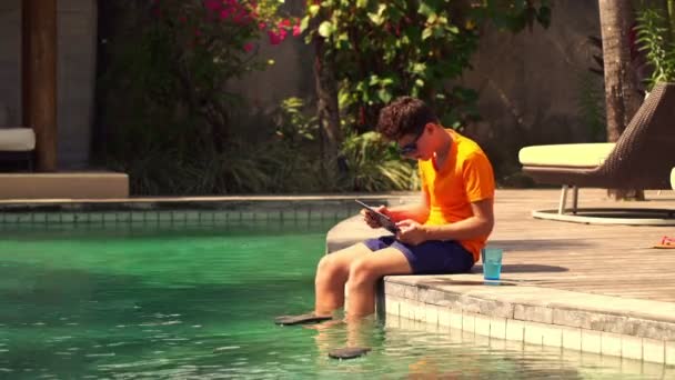 Teenager playing on tablet by edge of swimming pool — Stock Video