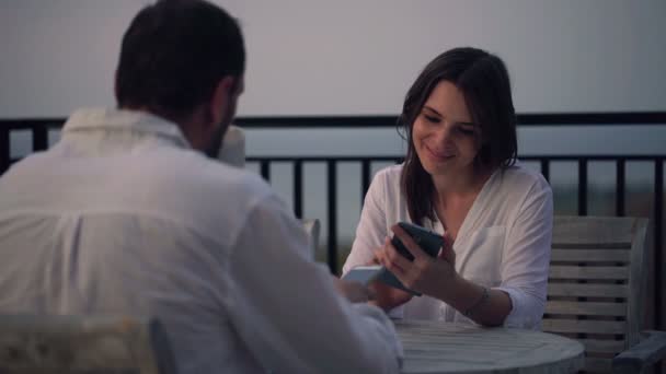 Pareja con smartphone sentado por la mesa en la terraza — Vídeo de stock