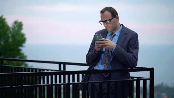Hombre de negocios mensajes de texto en el teléfono inteligente en la terraza — Vídeo de stock