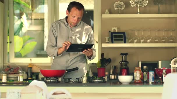 Hombre con la computadora de la tableta cocinar y agregar condimentos — Vídeo de stock