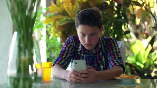 Adolescent textos sur smartphone assis à table — Video