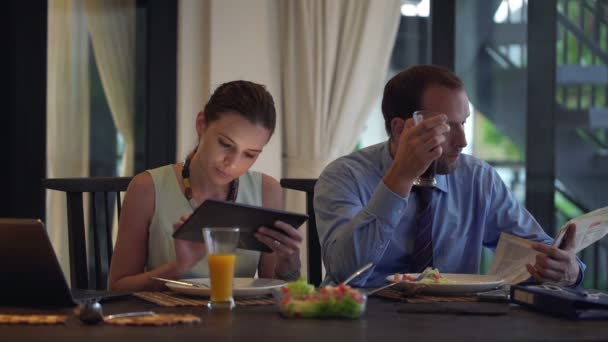 Пара використовує планшетний комп'ютер, читає газету та їсть — стокове відео