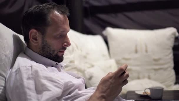 Man verzenden sms op smartphone op bed — Stockvideo