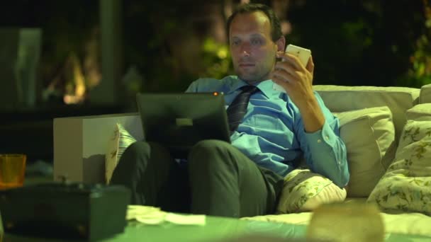 Бизнесмен работает со смартфоном и ноутбуком на диване — стоковое видео