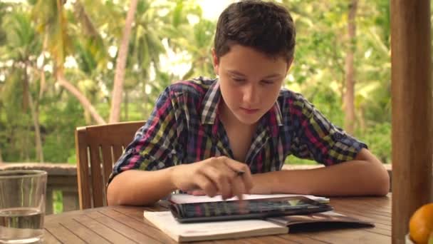 Підліток робить домашнє завдання і використовує планшетний комп'ютер — стокове відео