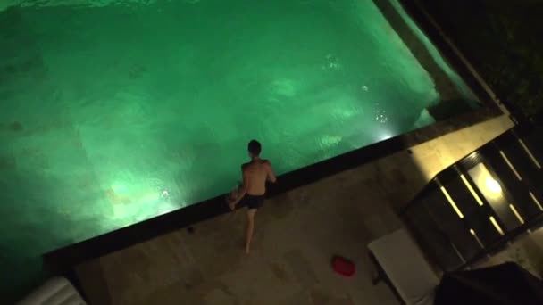 Teenager jumping into swimming pool at night — Stock Video