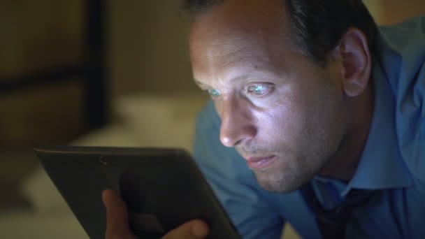 Человек смотрит фильм на планшетном компьютере на кровати — стоковое видео