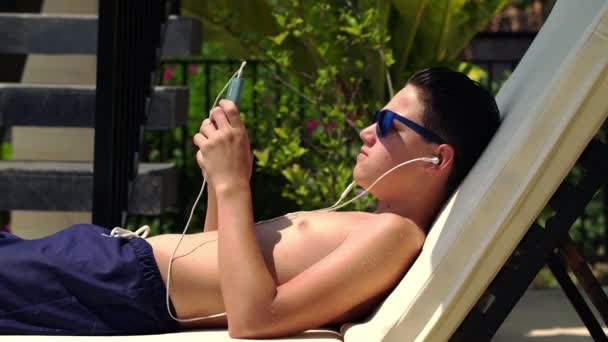 Teenager listen to music on sunbed — Stock Video