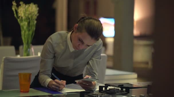 Бізнес-леді, що працює зі смартфоном і документами на кухні — стокове відео
