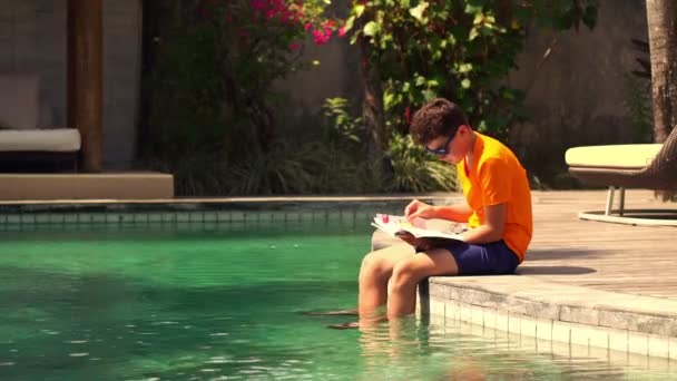 Teenager sitting with book on the edge of swimming pool — Stock Video