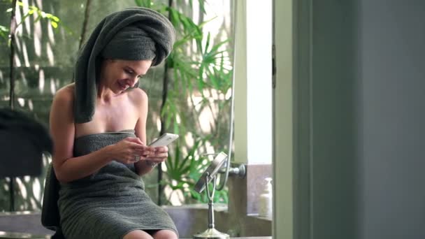 Woman with smartphone sitting in bathroom — Stock Video