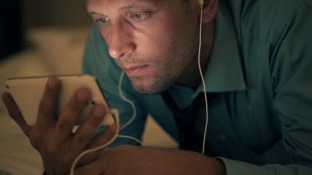 Hombre viendo vídeo en el teléfono inteligente en la cama — Vídeos de Stock