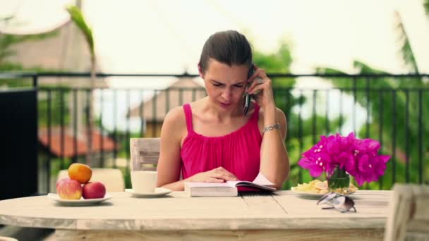 Mujer hablando por celular y explicando libro — Vídeo de stock