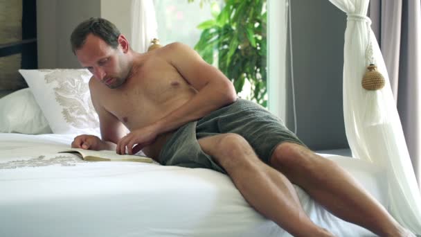 Young man reading book on bed — Stock Video