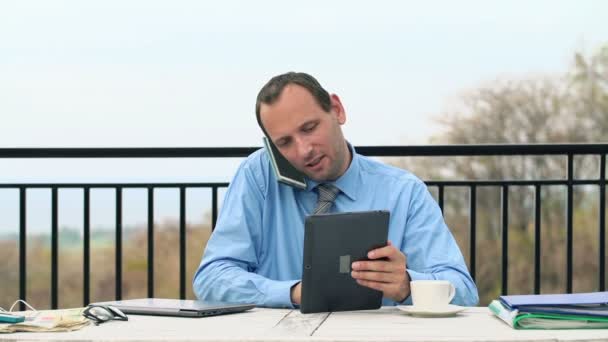 Бизнесмен разговаривает по мобильному телефону, смотрит на планшетный компьютер — стоковое видео