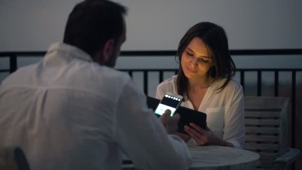 Pareja con smartphone y tablet sentados junto a la mesa — Vídeo de stock