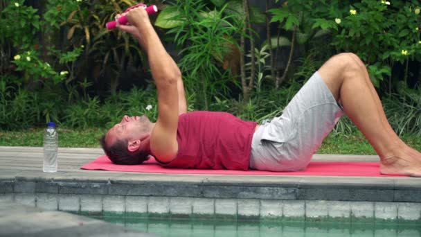 Hombre haciendo ejercicio con mancuernas en la alfombra en el jardín — Vídeo de stock