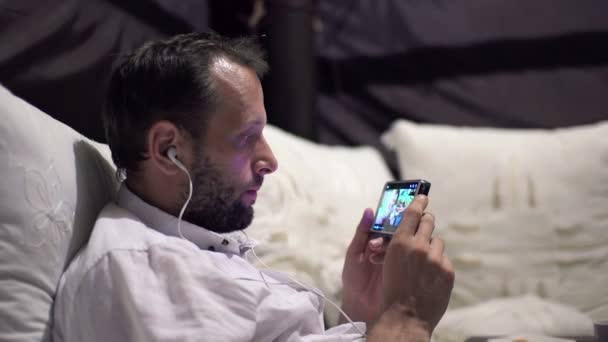 Man tittar på film på smartphone på sängen — Stockvideo