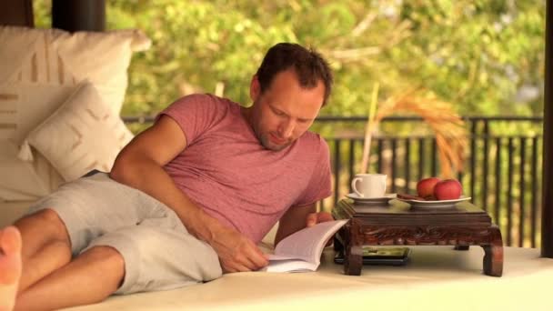 Hombre leyendo libro y comiendo galleta — Vídeo de stock